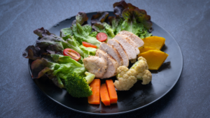 Talerz z różnorodnymi produktami spożywczymi dozwolonymi na diecie keto, w tym mięso, warzywa i tłuszcze zdrowe.